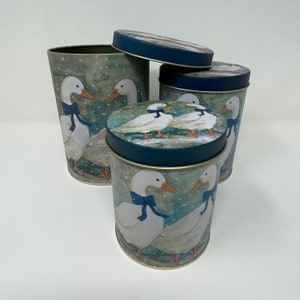 Peut inclure: Ensemble de quatre boîtes en céramique bleu et blanc avec une scène hivernale de canards. Les boîtes ont une bordure dorée et sont décorées d'un fond enneigé et de canards avec des rubans bleus.