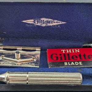Puede incluir: Juego de afeitadora Gillette vintage en un estuche azul. El juego incluye un mango de afeitadora plateado, un cabezal de afeitadora y una caja roja y blanca de cuchillas "Thin Gillette". El estuche tiene un interior de terciopelo azul y un logotipo de "Gillette".