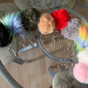 May include: A set of ten colourful fluffy pom pom keychains with silver key rings. The pom poms are in various colours, including black, blue, green, beige, red, grey, white, and pink.