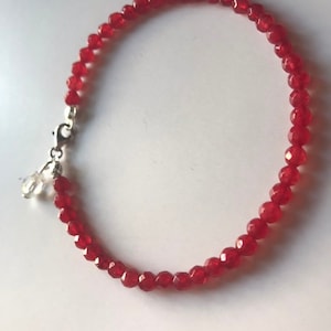 May include: A red beaded bracelet with a silver clasp and a small, clear crystal charm. The bracelet features small, faceted red beads. The clasp is silver and has a lobster claw closure.