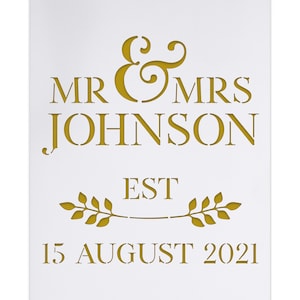 Può includere: Segno da matrimonio dorato con il testo "Mr & Mrs Johnson Est 15 agosto 2021" con un designo decorativo di ramo con foglie.