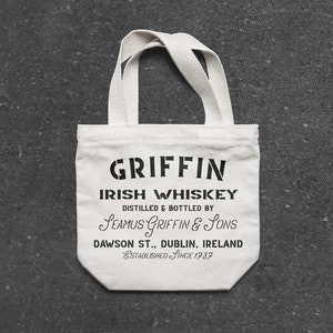 K&ouml;nnte beinhalten: Wei&szlig;e Stofftasche mit schwarzem Text, der "GRIFFIN IRISH WHISKEY DISTILLED & BOTTLED BY SEAMUS GRIFFIN & SONS DAWSON ST., DUBLIN, IRELAND ESTABLISHED SINCE 1787" lautet