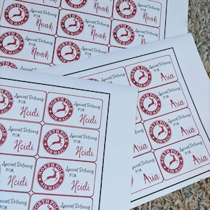 Puede incluir: Una hoja de papel blanco con varias etiquetas rojas y blancas de "North Pole Air Mail". Las etiquetas tienen un gr&aacute;fico de reno y el texto "Special Delivery for" seguido de un nombre. Los nombres en las etiquetas son Noah, Heidi y Aria.