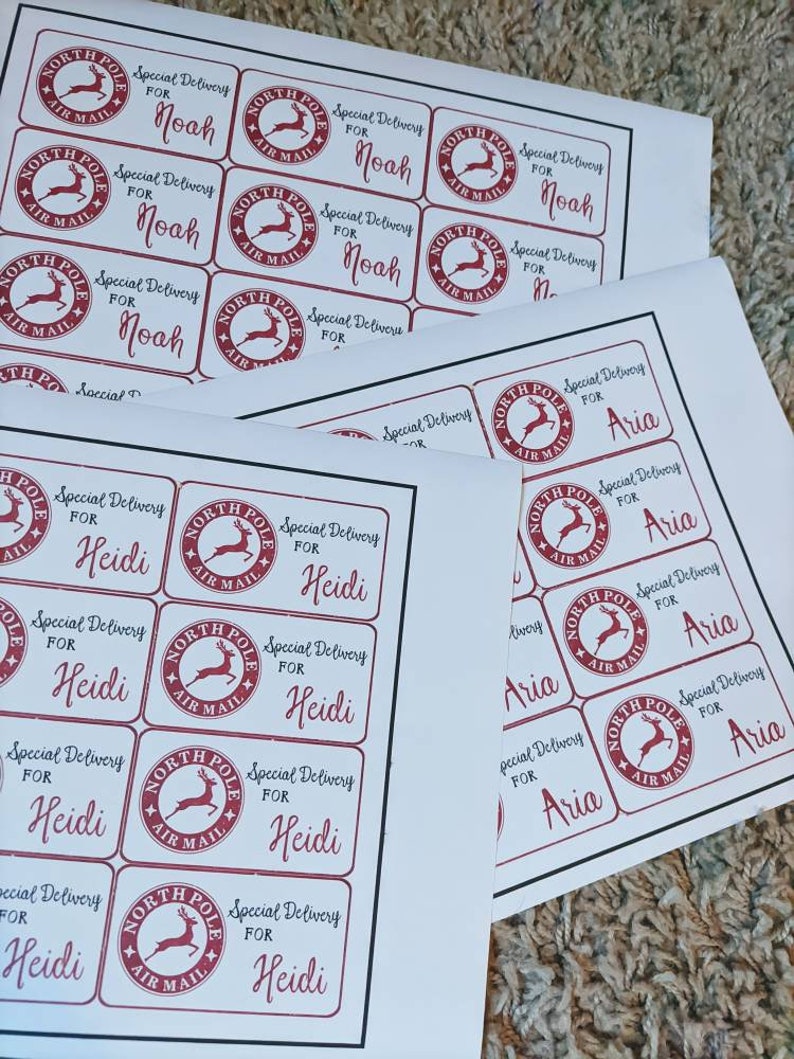 Puede incluir: Una hoja de papel blanco con varias etiquetas rojas y blancas de "North Pole Air Mail". Las etiquetas tienen un gr&aacute;fico de reno y el texto "Special Delivery for" seguido de un nombre. Los nombres en las etiquetas son Noah, Heidi y Aria.