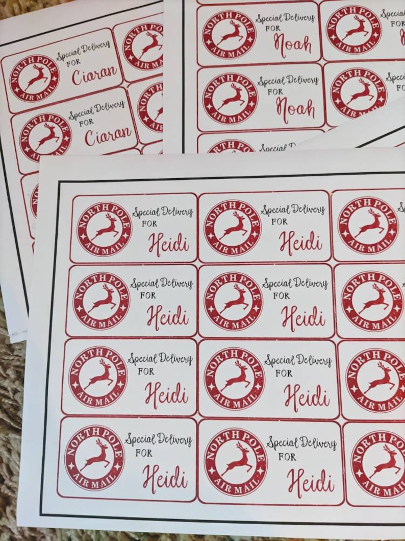 Puede incluir: Una hoja de papel blanco con etiquetas de regalo de Navidad rojas y blancas. Las etiquetas muestran un reno rojo con las palabras "North Pole Air Mail" y "Special Delivery" impresas en ellas. Las etiquetas est&aacute;n personalizadas con los nombres "Ciaran", "Noah" y "Heidi".