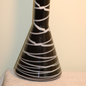 May include: A black glass vase with white stripes. The vase is tall and narrow with a rounded base.