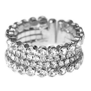 May include: A silver ring with three rows of clear rhinestones. The ring is adjustable and has a smooth, polished finish.