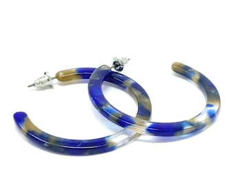 May include: A pair of blue and brown hoop earrings. The earrings are made of a marbled plastic material.