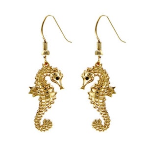 May include: Gold-tone dangle earrings featuring a detailed seahorse design. The seahorses have black eyes and are suspended from a hook.