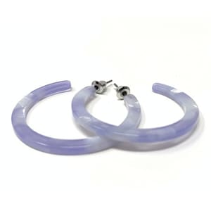May include: A pair of light purple hoop earrings with a marbled effect. The earrings are made of plastic and have silver-toned posts.