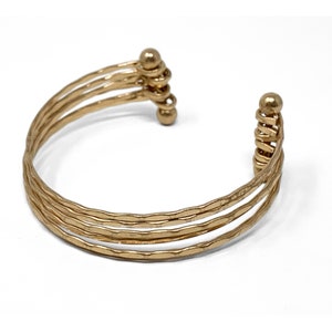 May include: Gold-toned multi-strand bangle bracelet with a hammered finish. The bracelet has a hinged closure with a ball detail.