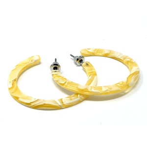 May include: A pair of yellow and white marbled hoop earrings with silver post backs.