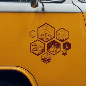 Może przedstawiać: Ż&oacute;łty van z brązowym konturem wzoru plastra miodu po bokach. Każdy sześciokąt we wzorze przedstawia inną scenę na świeżym powietrzu, w tym vana, g&oacute;ry, ognisko i księżyc.