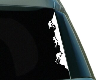 May include: White silhouette decal of a group of people rock climbing on a cliff face. The decal is applied to the back window of a car.