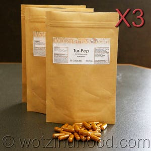 Op de afbeelding: Drie bruine papieren zakken met een wit etiket waarop "Tur-Pep Ontstekingsremmend Antioxidans 50 capsules 900mg" staat en een kleiner etiket met de tekst "Supplement Facts". De zakken staan op een grijs oppervlak met een stapel bruine capsules op de voorgrond.