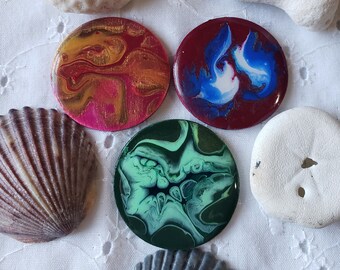 May include: Three round, colorful, abstract resin coasters with swirling patterns. The coasters are red, blue, and green with white accents.
