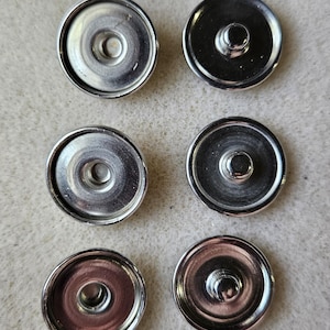 May include: Ten silver-toned metal snap buttons with a raised center. The buttons are arranged in two rows of five.