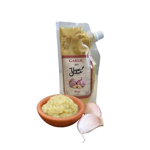 May include: A pouch of garlic paste with the brand name "Yape! Gourmet" and the text "Garlic Ajo Paste" on the front. The pouch is next to a small bowl of garlic paste and two cloves of garlic.