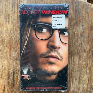 May include: A DVD case featuring Johnny Depp on the cover. The title of the movie is "Secret Window" and the text "Some windows should never be opened." is at the bottom of the case.