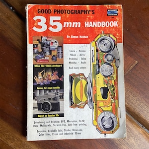 May include: A vintage book cover with a red background and the title "GOOD PHOTOGRAPHY'S 35mm HANDBOOK" in white text. The cover features a cutaway illustration of a 35mm camera with the text "Leica, Konica, Nikon, Aires, Praktina, Edixa, Minolta, Asahi, and many others" listed below.