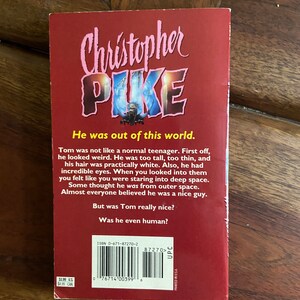 Może przedstawiać: Czerwona książka w miękkiej oprawie z tytułem "Christopher Pike" w r&oacute;żowych literach. Okładka książki przedstawia czarno-białą ilustrację osoby o przerażającym wyrazie twarzy. Tekst na tylnej stronie książki brzmi: "Był poza tym światem." i "Tom nie był jak normalny nastolatek. Po pierwsze, wyglądał dziwnie. Był za wysoki, za chudy i jego włosy były prawie białe. Poza tym miał niesamowite oczy. Kiedy patrzyłeś w nie, czułeś się, jakbyś wpatrywał się w głęboką przestrzeń kosmiczną. Niekt&oacute;rzy myśleli, że pochodzi z kosmosu. Prawie wszyscy wierzyli, że jest miłym chłopakiem. Ale czy Tom był naprawdę miły? Czy był w og&oacute;le człowiekiem?" Numer ISBN to 0-671-87270-2.