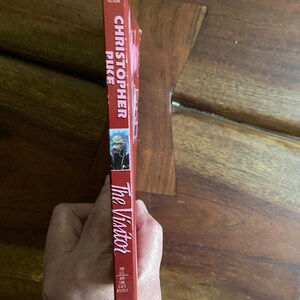 Może przedstawiać: Czerwona książka w miękkiej oprawie zatytułowana "The Visitor" autorstwa Christophera Pike'a. Książka jest częścią serii Archway Paperback Fiction.