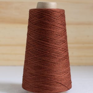 May include: A spool of brown thread, tightly wound around a cardboard core. The thread has a smooth texture and a rich, earthy tone. The spool is set against a light wooden background, highlighting the thread's color and texture. Ideal for sewing and crafting projects.