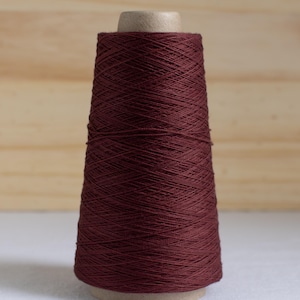 May include: A spool of burgundy-colored thread. The thread is tightly wound around a cardboard core, creating a conical shape. The thread has a smooth, slightly shiny texture, and the overall appearance is neat and organized. Ideal for sewing and crafting projects.
