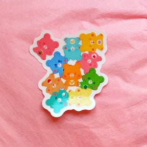 May include: A sticker sheet featuring nine colorful cartoon bears with different facial expressions and symbols on their bellies. The bears are arranged in a cluster, with their heads facing outward.