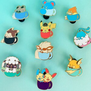 May include: A set of ten enamel pins featuring various Pokemon characters in a teacup. The pins are gold-toned and feature a variety of colors, including blue, red, yellow, green, and purple.
