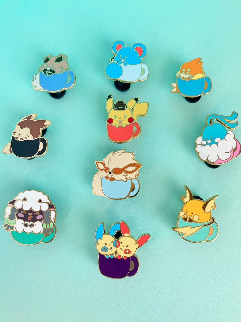 May include: A set of ten enamel pins featuring various Pokemon characters in a teacup. The pins are gold-toned and feature a variety of colors, including blue, red, yellow, green, and purple.