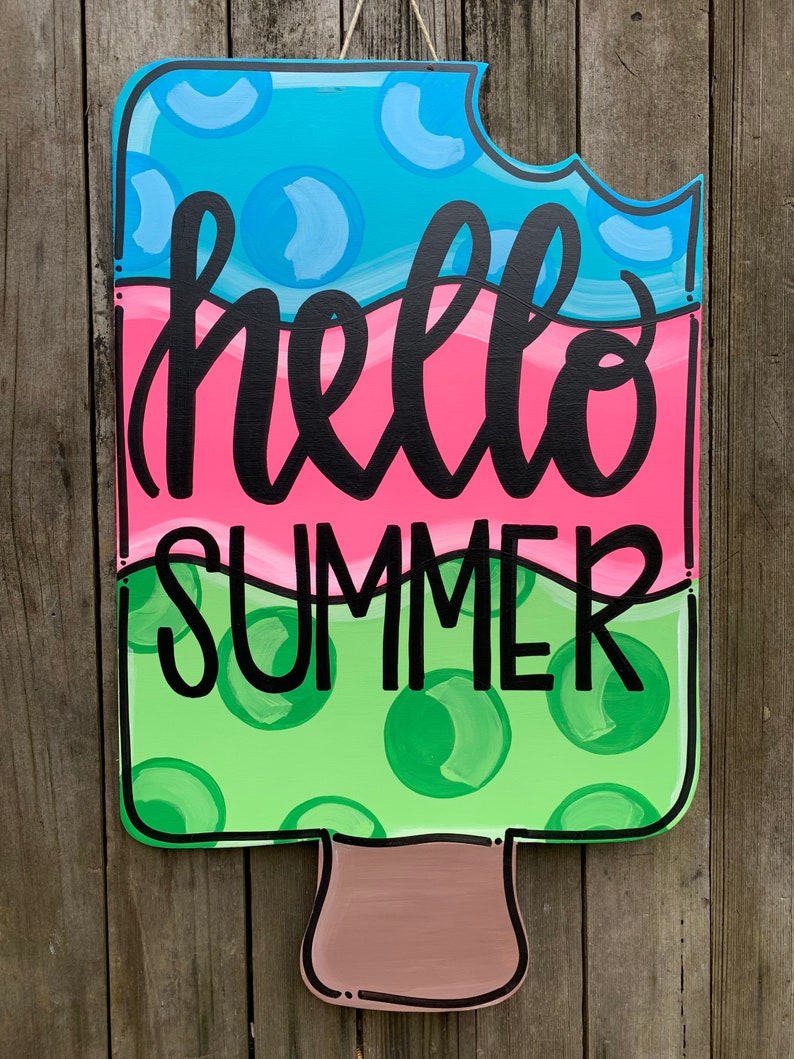 May include: A wooden popsicle door hanger with a blue, pink, and green color scheme. It has a bite taken out of the top and says "hello summer" in black lettering.