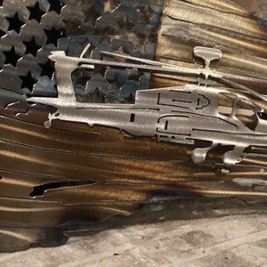 May include: A metal sculpture of an American flag with a helicopter cut out of the center. The flag is distressed and has a rustic look. The helicopter is in flight and has a detailed design.