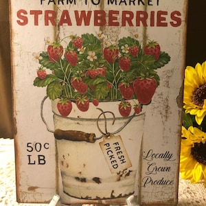 Może przedstawiać: Tabliczka w stylu vintage z napisem "Farm to Market Strawberries" w czerwonych literach. Tabliczka ma białe tło z efektem zużycia i obraz wiaderka ze świeżymi truskawkami z zielonymi liśćmi i białymi kwiatami. Wiaderko ma etykietę z napisem "Fresh Picked". Tabliczka zawiera r&oacute;wnież tekst "50c LB" i "Locally Grown Produce".