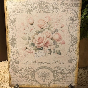 May include: A vintage-style wooden plaque with a floral design featuring pink roses and a bee. The plaque has a distressed, aged look and features the text "Belle Rose" and "Le Bouquet de Roses".