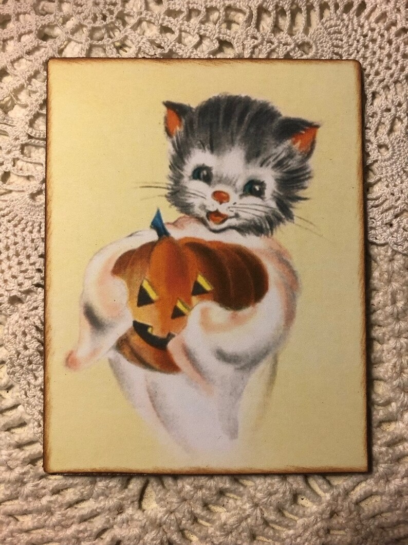 Pu&ograve; includere: Un'illustrazione vintage di Halloween di un gatto grigio e bianco che tiene una zucca arancione intagliata. Il gatto indossa un costume da fantasma bianco e ha un'espressione felice sul viso.
