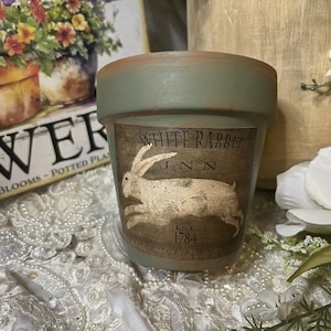 May include: A small green terracotta flower pot with a brown label that says "White Rabbit Inn Est. 1784" and a white rabbit illustration.