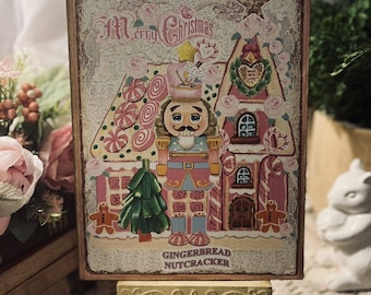May include: A vintage-style Christmas card featuring a gingerbread house with a candy cane trim and a gingerbread nutcracker standing in front of it. The card has a pink and white color scheme and says "Merry Christmas" and "Gingerbread Nutcracker" in gold lettering.