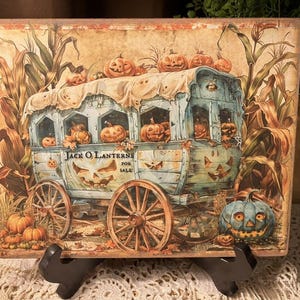 May include: A rectangular wooden sign featuring a vintage illustration of a wagon filled with carved pumpkins. The wagon is light blue with wooden wheels, and the sign reads "Jack O'Lanterns For Sale". The background includes corn stalks and a large blue pumpkin.