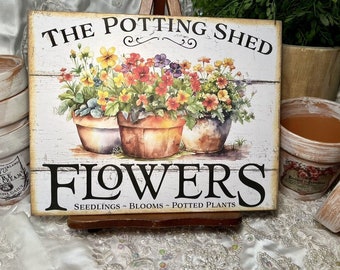 May include: White wooden sign with the text "The Potting Shed Flowers Seedlings - Blooms - Potted Plants". The sign features a watercolour illustration of three potted plants with colourful flowers.