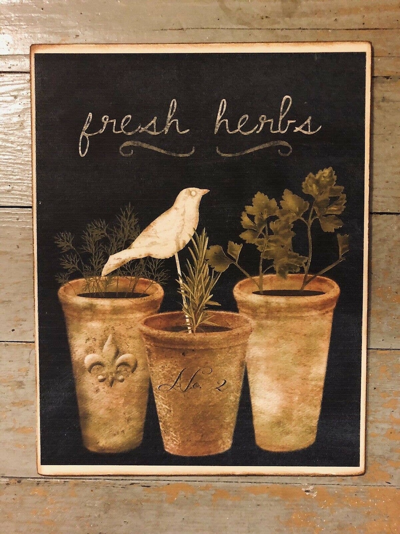 May include: A black chalkboard sign with the text "fresh herbs" in white script. Three terracotta pots with different herbs are arranged in a row. A white bird sits on a branch in the center pot. The pots are labeled with a fleur-de-lis and the number "2".