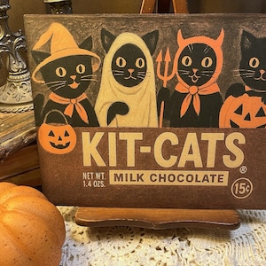 May include: A vintage-style Halloween-themed sign featuring four black cats in costumes. The sign reads "KIT-CATS" with "MILK CHOCOLATE" below. The net weight is 1.4 ounces. The cats are dressed as a witch, ghost, devil, and pumpkin.