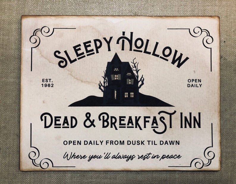 May include: A vintage-style sign with the text "Sleepy Hollow Dead & Breakfast Inn" in a spooky font. The sign features a silhouette of a haunted house with windows and a black background. The text "Est. 1962" and "Open Daily" are also included.
