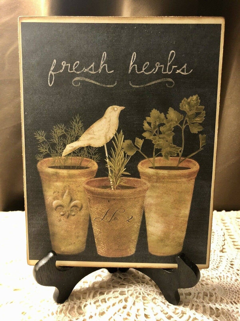 May include: A black chalkboard with the text "fresh herbs" in white script. The chalkboard features a white bird perched on a rosemary plant in a terracotta pot. Two other terracotta pots with herbs are visible, one labeled "No. 2".