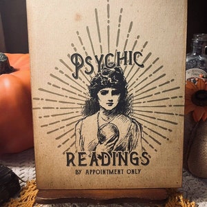 May include: A vintage-style sign with a black and white illustration of a woman with a crystal ball. The sign reads "Psychic Readings by Appointment Only".