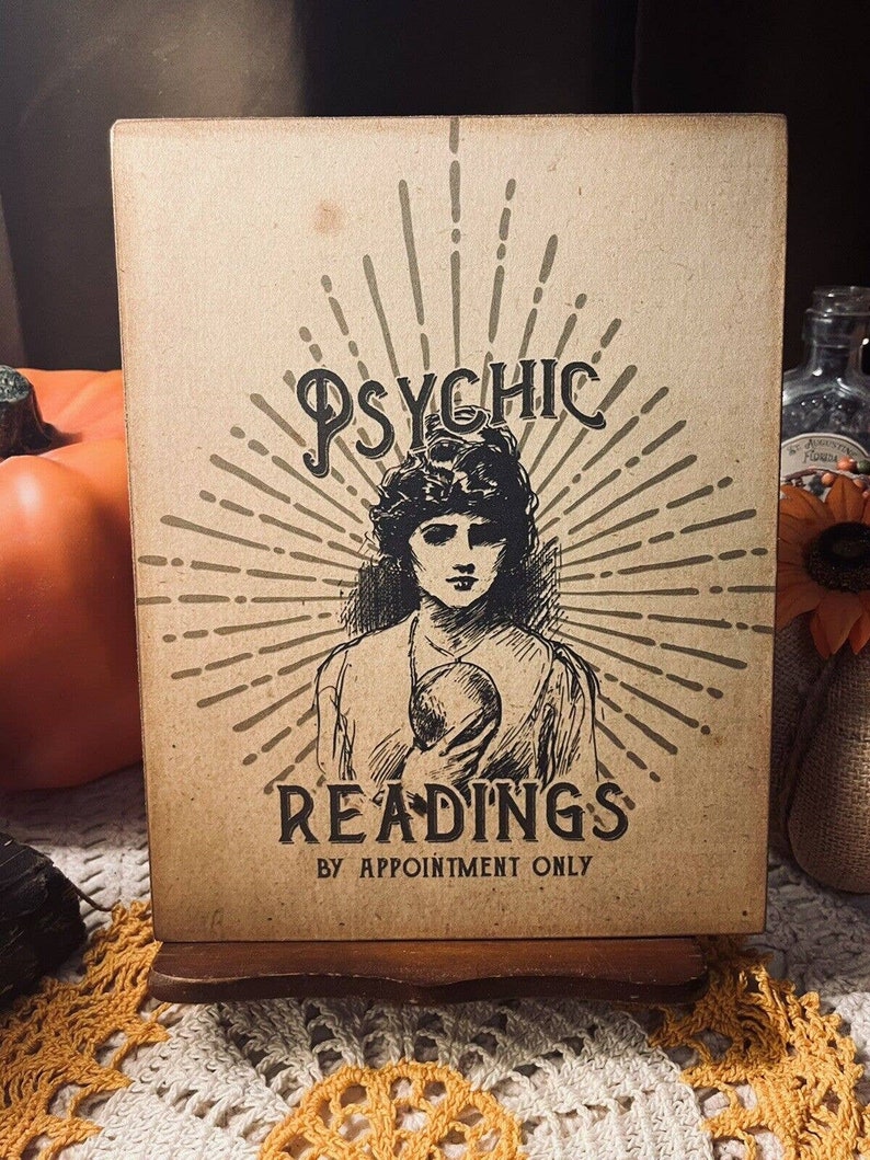 May include: A vintage-style sign with a black and white illustration of a woman with a crystal ball. The sign reads "Psychic Readings by Appointment Only".