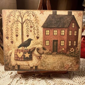 May include: A rectangular decorative wooden plaque featuring a folk art scene. It depicts a house, a sheep with a crow on its back, and a weeping willow tree. The color palette includes shades of brown, beige, and red.