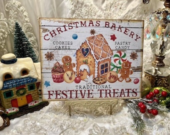 May include: A white wooden sign with the text "Christmas Bakery" in red letters. The sign features a gingerbread house, cookies, cakes, candy, and the text "Traditional Festive Treats".