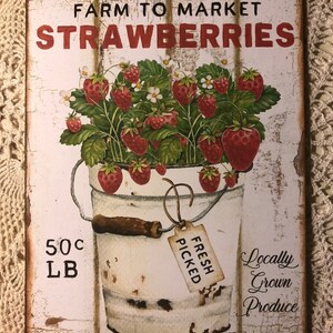 Może przedstawiać: Biały metalowy znak z czerwonym napisem "Farm to Market Strawberries". Znak przedstawia vintage'ową ilustrację wiadra przepełnionego czerwonymi truskawkami i zielonymi liśćmi. Wiadro ma drewniany uchwyt i etykietę z napisem "Fresh Picked". Znak zawiera r&oacute;wnież tekst "50c LB" i "Locally Grown Produce".