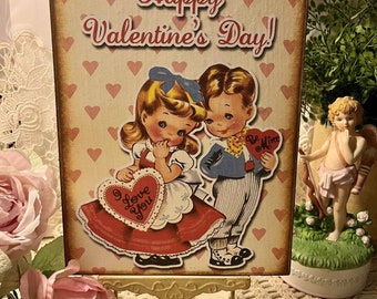 Può includere: Un biglietto di San Valentino in stile vintage con un motivo a cuori rosa e bianchi. Il biglietto presenta un'illustrazione di cartoni animati di un ragazzo e una ragazza che tengono in mano biglietti a forma di cuore che dicono "Be Mine" e "I Love You". Il biglietto recita "Happy Valentine's Day!"
